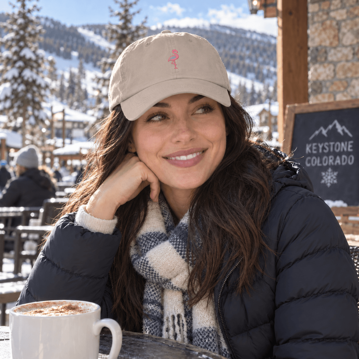 Brunette woman wearing a Stone Frosty Flamingo dad cap outside a snowy mountain café